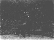 Portrait d'un homme à la moustache et au canotier, assis sur une chaise de jardin