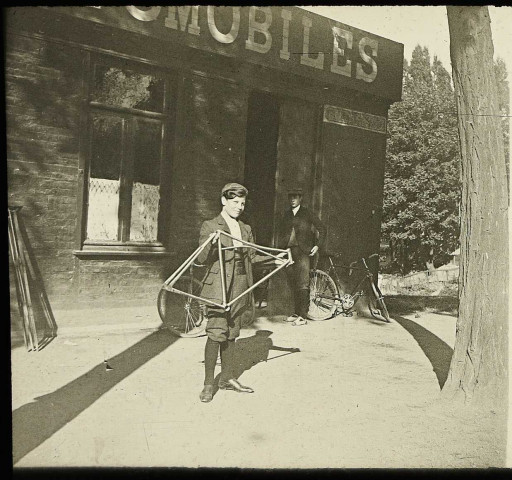 Amiens (Somme). Un jeune garçon tenant un cadre de vélo devant un magasin de cycles