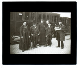 [Groupe d'hommes sur le quai d'une gare suisse. Au second plan, un wagon avec une mention "Fumeurs"]