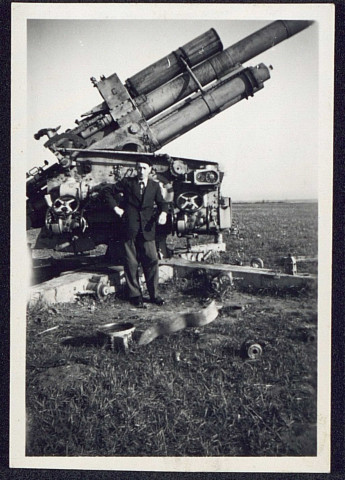 Un homme en costume posant devant un canon allemand antiaérien de 88 mm