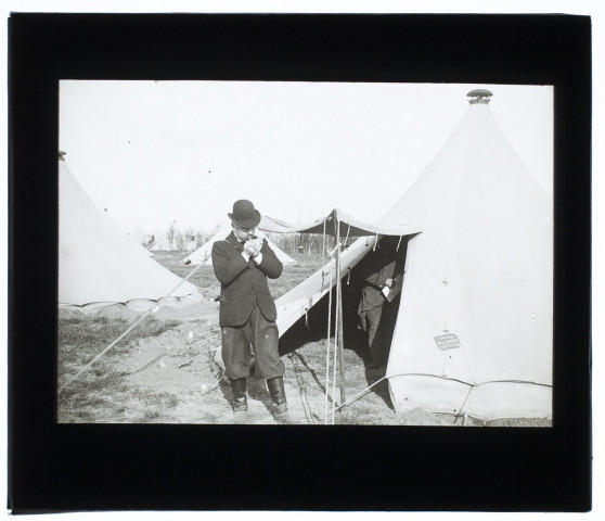 [Manoeuvres militaires : les tentes des officiers du camp de Sissonne. Un homme avec un chapeau melon allume une cigarette devant la tente du Lieutenant de Santeul]