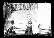 Amiens. Deux femmes et une fillette portant un canapé en osier dans un jardin