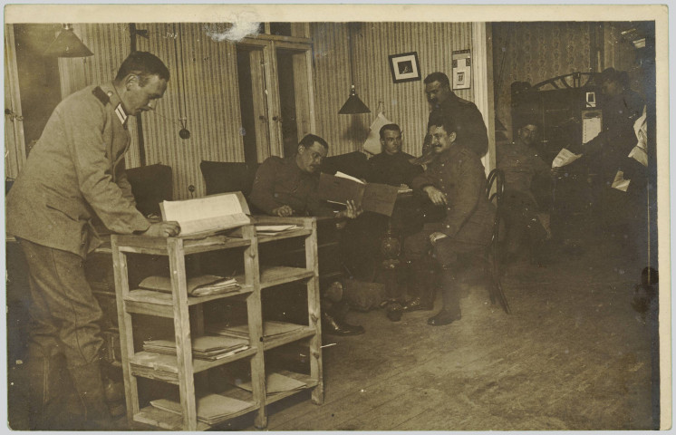 CARTE-PHOTO MONTRANT SEPT SOLDATS ALLEMANDS DANS UNE PIECE, CONSULTANT DES DOCUMENTS. SOMBRE. PAPIER COLLE BORD SUPERIEUR GAUCHE