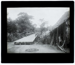 [Un habitant malgache devant une cabane traditionnelle - pont de bois]
