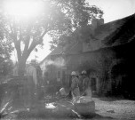 Groupe de trois personnes dans une cour devant une maison de village (fontaine et linge à laver)