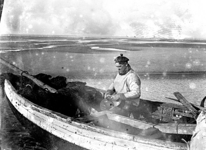 Paysage littoral. Un pêcheur débarquant son canot de pêche sur la plage