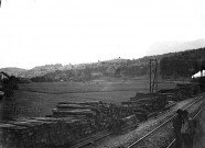Environs de Berne (Suisse). Travaux sur une voie ferrée : averses en bois entreposées le long d'une voie. Au fond à droite, un train à vapeur. Au second plan, un paysage de montagne
