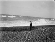 Paysage du littoral : portrait d'homme et son chien sur la plage de galets, devant une tempête