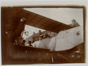 Photographie montrant un homme et une femme en chapeau à bord d'un avion Zodiac 2S. Deux autres hommes en chapeau à côté du biplan. Bâtiment en briques en arrière plan