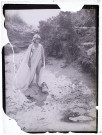 [Mise en scène artistique du photographe : une femme à moitié dénudée portant un drapée antique et regardant une amphore posée sur le sable