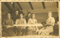 Prisonniers de guerre assis dans un baraquement du Stalag VIII-C. Louis Delignières est penché entre les deux prisonniers assis au centre