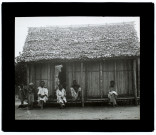 [Groupe de malgaches assis devant une cabane traditionnelle]