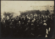 Photographie montrant la cérémonie d'inauguration du monuments aux Morts de Neuville-Vitasse. Foule devant les marches d'un bâtiment, prise depuis la droite. Au premier plan, de nombreuses femmes, les hommes à l'arrière et à droite. Au centre, un enfant. En arrière plan, une pâture avec une vache