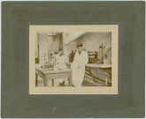 PHOTOGRAPHIE MONTRANT ALBERT RISER, PHARMACIEN MILITAIRE (PERE DE MARCEL RISER) DANS UN LABORATOIRE. COLLEE SUR CARTON (170 MMHT , 212 MMLA). RISER Albert (1850-1933). Père de Marcel Riser. Pharmacien militaire. Brillants états de services et décorations acquises au Tonkin