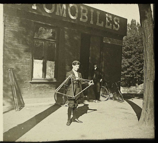 Amiens (Somme). Un jeune garçon tenant un cadre de vélo devant un magasin de cycles