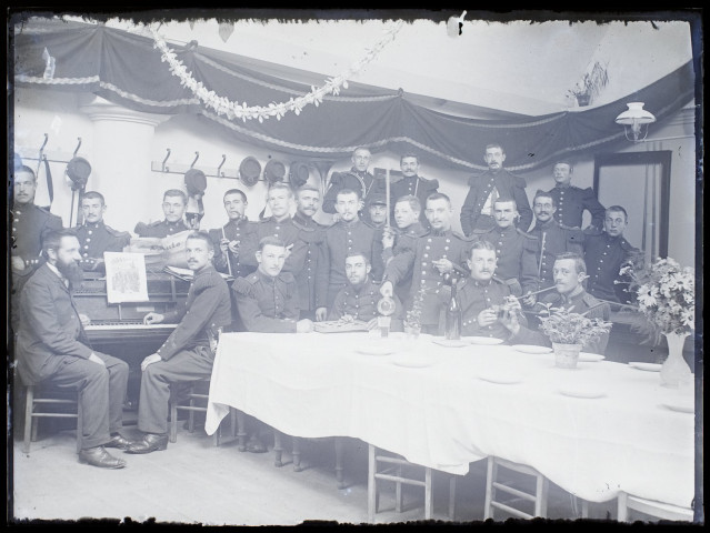 [Groupe de soldats posant lors de la célébration d'un événement. A gauche un pianiste jouant une partition "1804 - Marche Française". A droite, une table est dressée pour le repas]