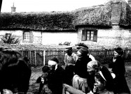 Scène villageoise. Un groupes de paysans devant une maison appareillée de briques et galets et couverte de chaume