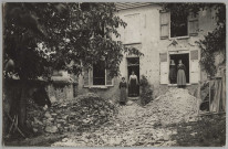 CARTE PHOTO MONTRANT DEUX FEMMES SUR LE PAS D'UNE PORTE ET DEUX JEUNES FILLES SUR LE BORD D'UNE FENETRE D'UNE MAISON AYANT SUBI LES BOMBARDEMENTS. TAS DE PIERRES DEVANT LA MAISON