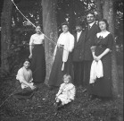 Groupe de cinq personnes debout le long d'arbres dans une forêt avec une jeune femme assise à l'extrémité gauche du groupe et une jeune fille assise au centre du groupe