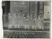[Cinq soldats en uniforme devant une grande porte en bois comportant une pancarte "Abri du soldat". Derrière, un homme regarde par la fenêtre]