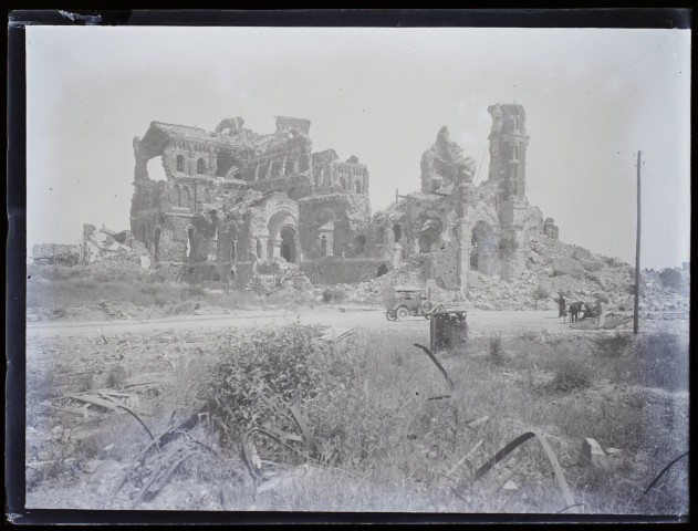 [Bâtiment détruit par les bombardements durant la première guerre mondiale. Une automobile est stationnée devant les ruines et à droite on distingue des personnages assis dont des femmes avec des ombrelles]