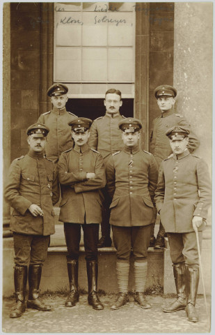 CARTE-PHOTO MONTRANT LE PORTRAIT DE SEPT OFFICIERS ALLEMANDS, EN PIEDS. CELUI A L'EXTREME DROITE EST AVEC UNE CANNE. NOMS MANUSCRITS AU CRAYON. AYANT APPARTENU A MONSIEUR LANGFELD