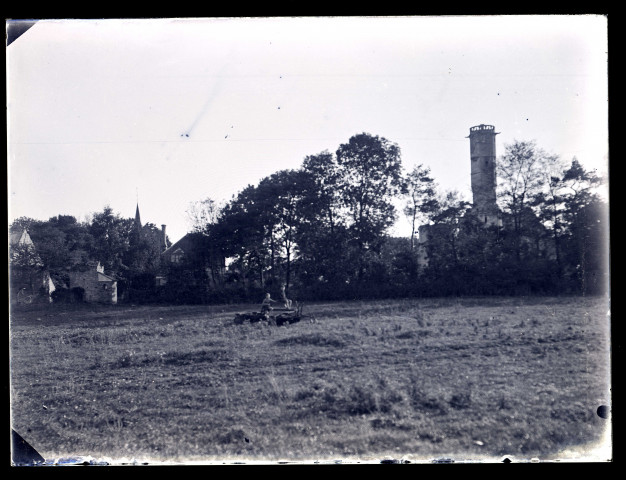 Deux garçons assis sur une machine agricole dans un champ. Au second plan, la tour du château de Folleville