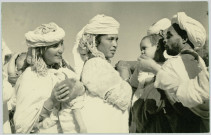 CARTE-PHOTO MONTRANT UNE FAMILLE D'INDIGENES MAROCAINS. LES FEMMES PORTANT LEUR BEBE SUR LE DOS. ECRITE DE "CASA" LE 27 JUIN 1956