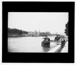 [Sur les bords de Seine : pêcheurs et bateaux mouches. Au fond, on distingue la silhouette de la Tour Eiffel et sur l'autre berge les préparatifs pour l'exposition universelle de 1900]