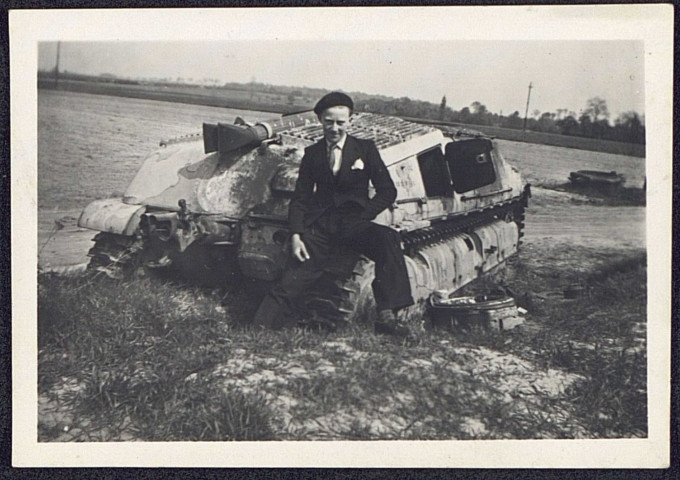 Un homme en costume posant devant les vestiges d'une chenillette de l'armée allemande