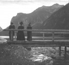 Vue sur un lac en montagne avec 3 personnes sur un pont