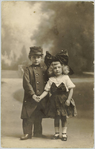 CARTE-PHOTO MONTRANT DEUX JEUNES ENFANTS SE DONNANT LA MAIN HABILLES, ELLE EN ALSACIENNE, LUI EN SOLDAT FRANCAIS 1914