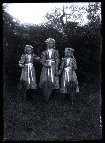 Scène de la vie quotidienne d'une famille bourgeoise. Trois jeunes filles en robes écossaisses dans un jardin