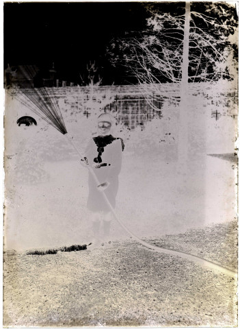 Un jeune garçon, Henri, tenant un tuyau d'arrosage