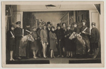 Amiens. Scène d'une pièce de théâtre. Quatorze acteurs posent devant un décor représentant une rue. Lucien Pilette est le cinquième à partir de la gauche. Des acteurs sont vêtus d'un costume de gendarme et deux d'entre-eux montent des chevaux factices