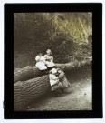 [Enfants assis ou jouant près d'un tronc d'arbre abattu]
