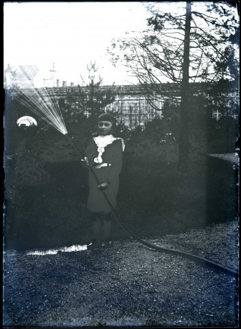 Un jeune garçon, Henri, tenant un tuyau d'arrosage